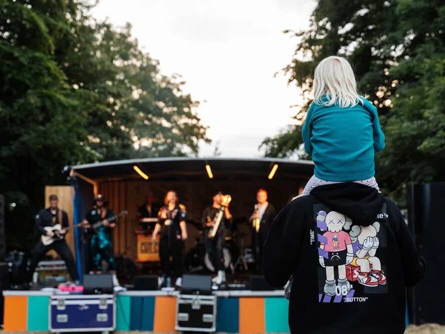 A child on their parent's shoulders watching a live band on an outdoor stage