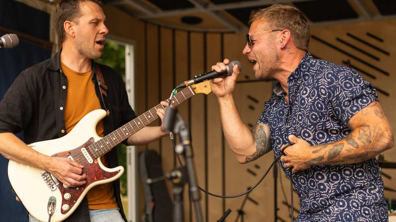 A guitarist and singer performing together on an outdoor stage